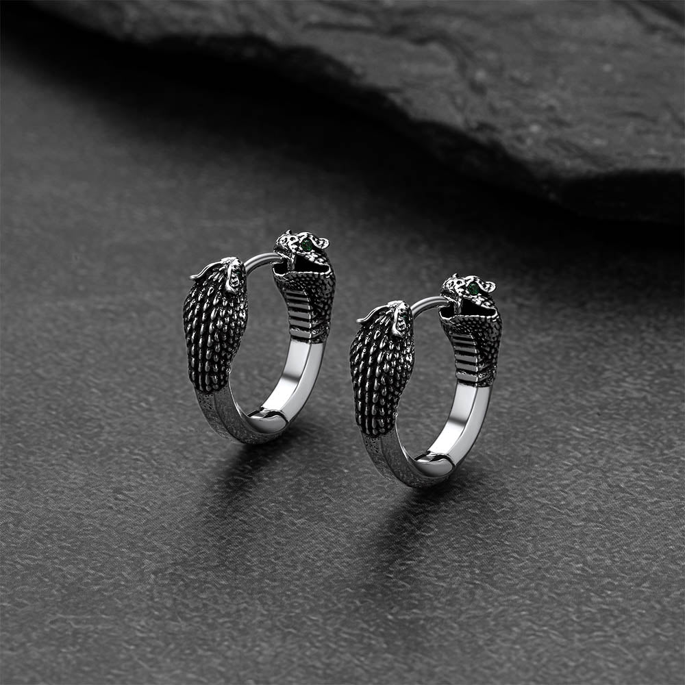 Pair of silver hoop earrings with snake designs on a dark surface