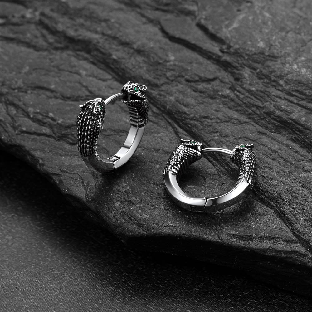 Pair of silver hoop earrings with snake designs on a dark stone surface