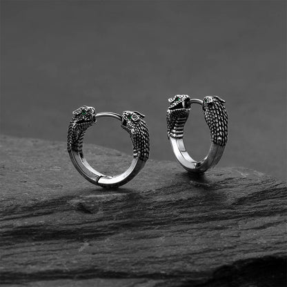 Pair of silver hoop earrings with snake head designs on a dark stone surface.