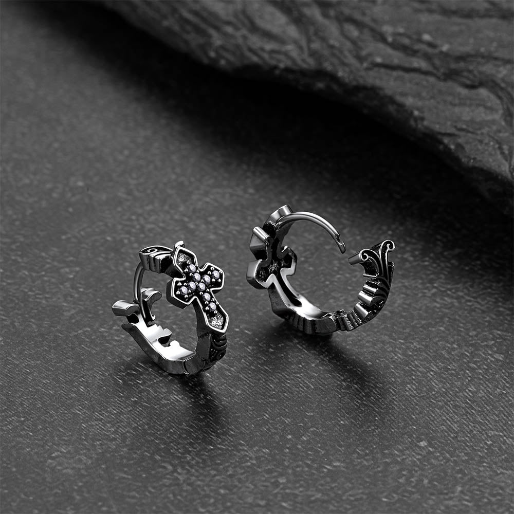 Pair of silver hoop earrings with cross designs on a dark surface