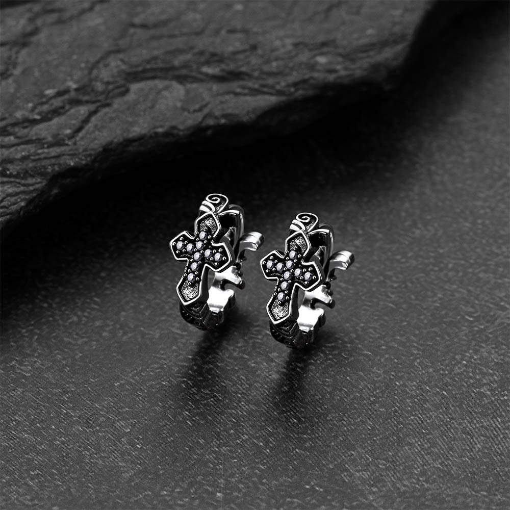 Pair of silver cross earrings on a dark stone surface