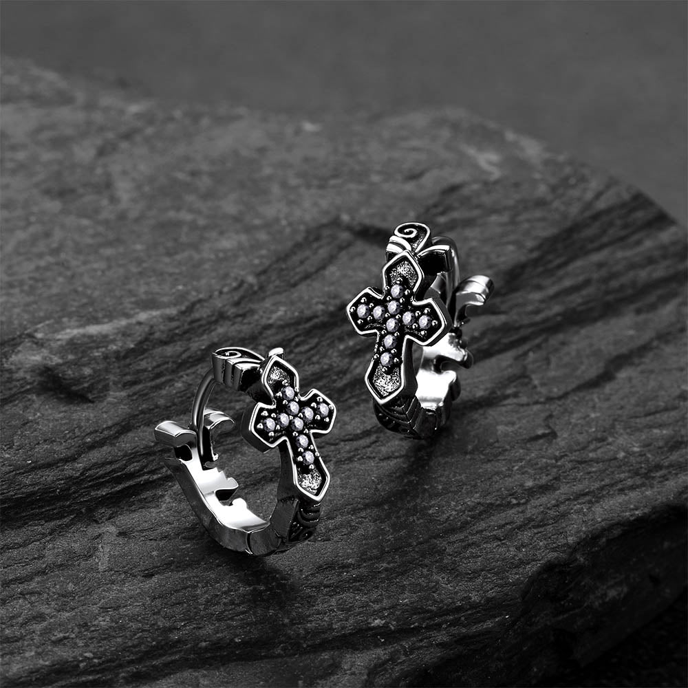 Pair of silver cross-shaped hoop earrings on a dark stone surface