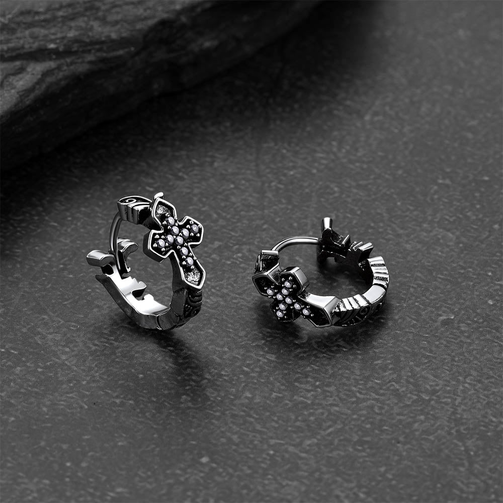 Pair of silver hoop earrings with cross designs on a dark surface