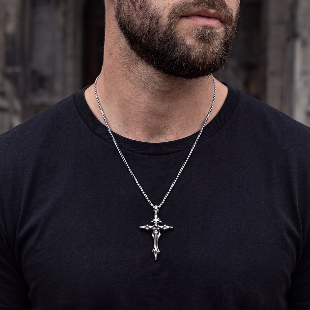 A close-up of a man wearing a silver crucifix cross pendant necklace on a black t-shirt.