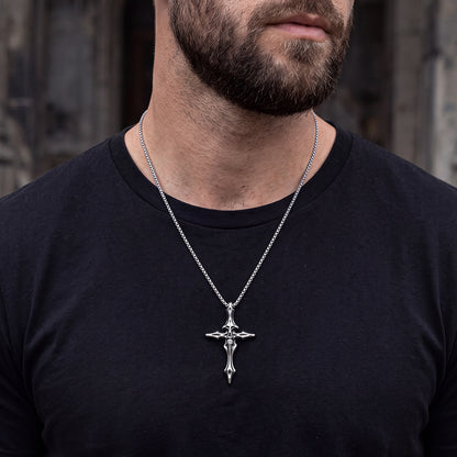 A close-up of a man wearing a silver crucifix cross pendant necklace on a black t-shirt.