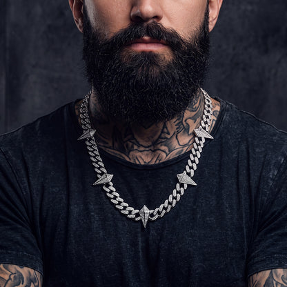 A close-up of a man wwearing a chunky silver chain necklace with pyramid-shaped links.