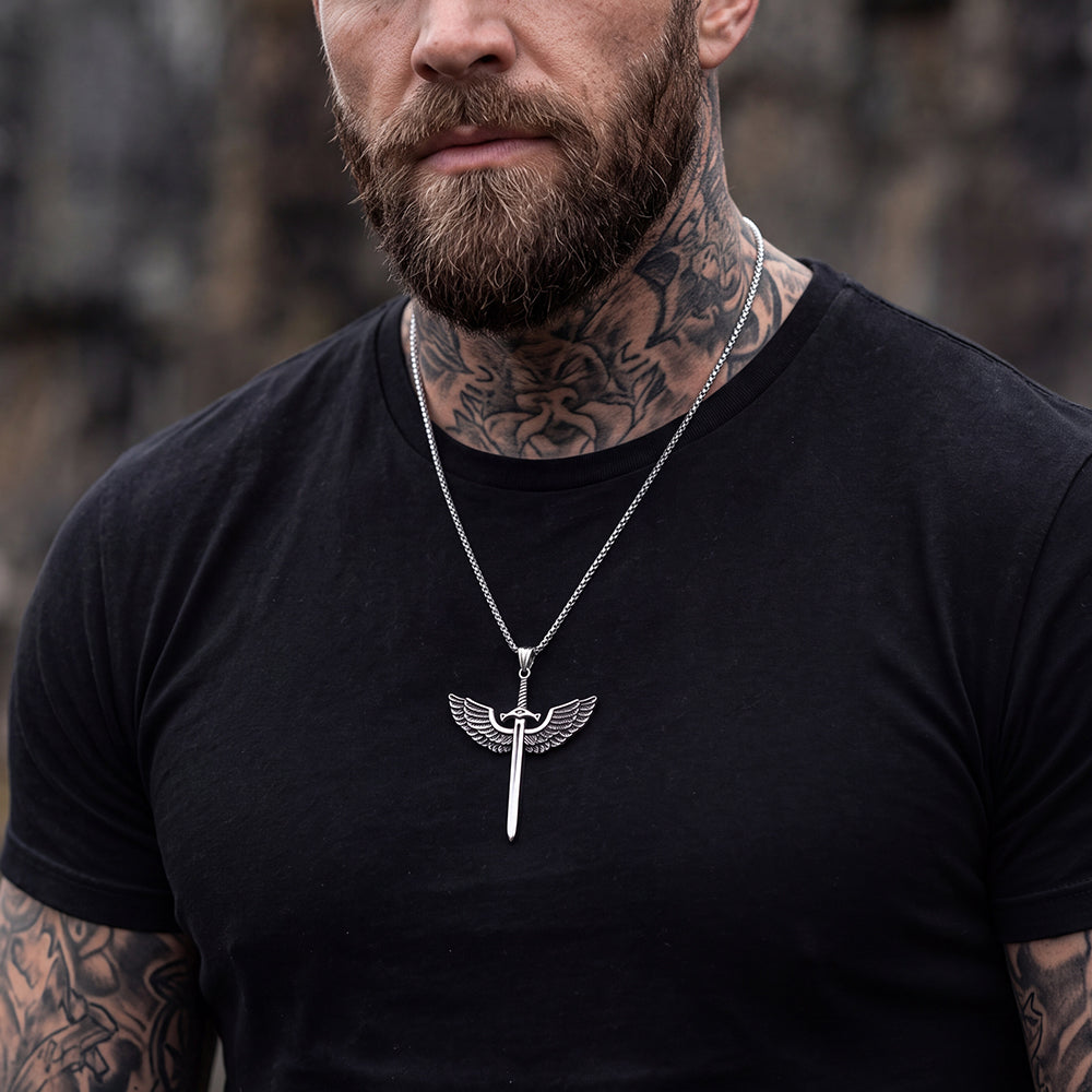 A close-up of a man wearing a silver winged pendant necklace over a black t-shirt.