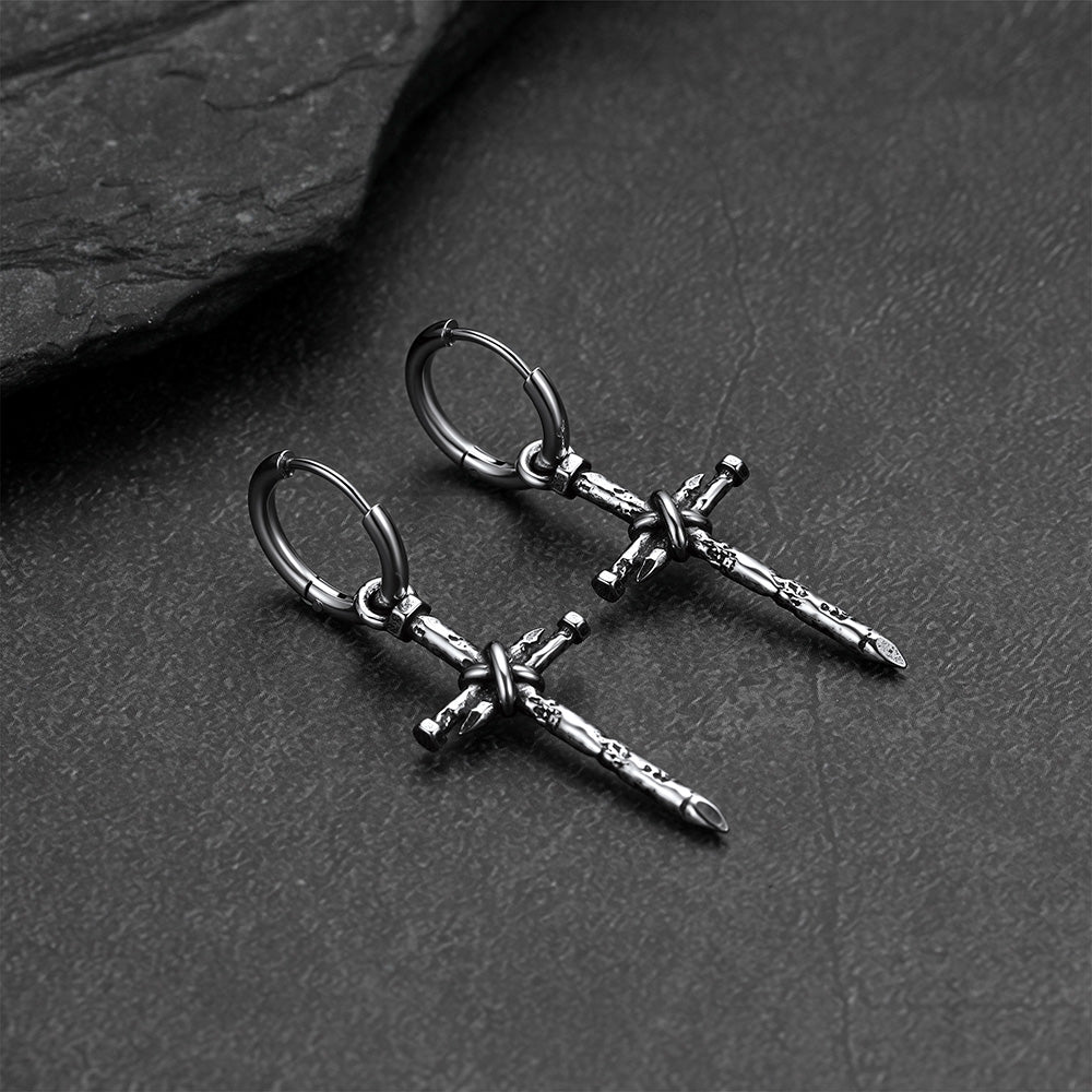 A pair of silver-toned cross drop hoop earrings displayed on a dark textured slate surface.