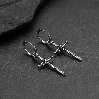 A pair of silver-toned cross drop hoop earrings displayed on a dark textured slate surface.
