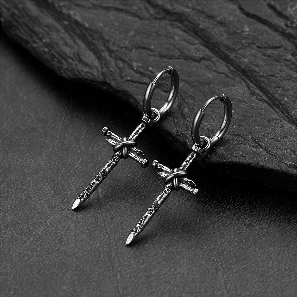A pair of gothic cross earrings on a dark textured slate surface.