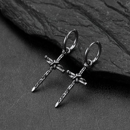 A pair of gothic cross earrings on a dark textured slate surface.