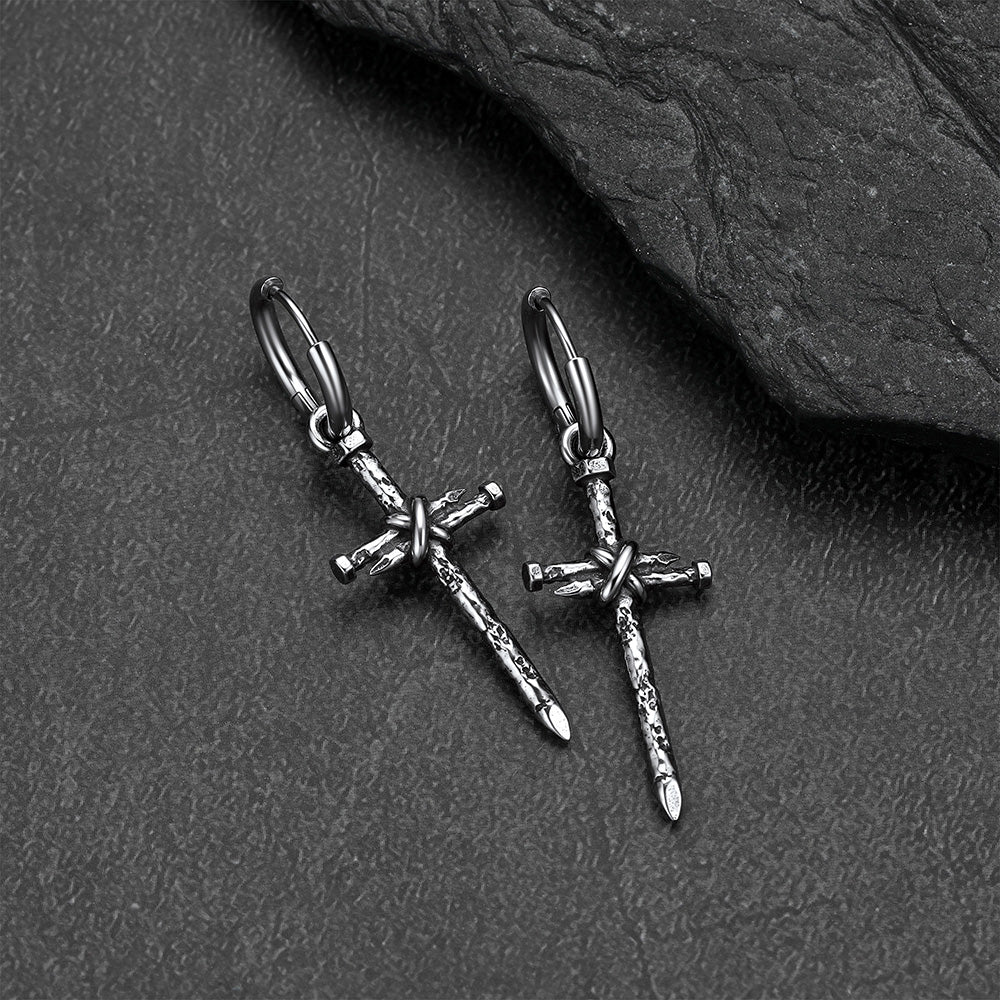 A pair of silver-toned gothic cross earrings, displayed on a dark textured slate surface.