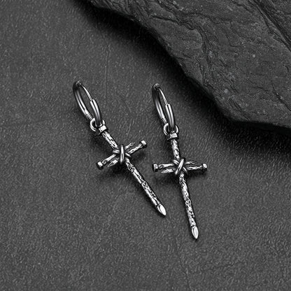 A pair of silver-toned gothic cross earrings, displayed on a dark textured slate surface.