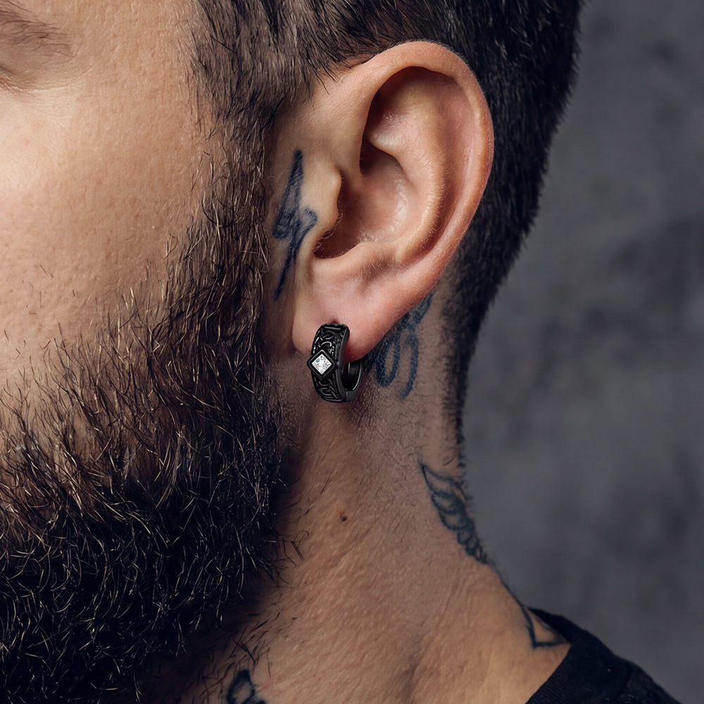 Close-up of a man's ear with a black earring, showcasing tattoos on his neck and jawline.