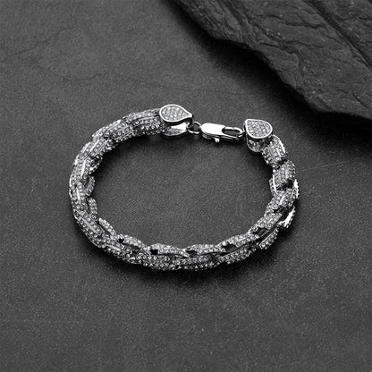 A silver-toned chain link bracelet with pavé-set clear stones, displayed on a dark textured surface with a black slate prop.