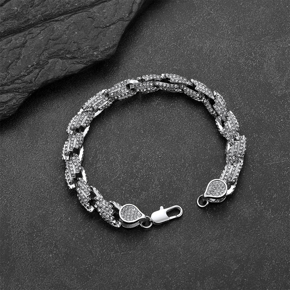 A silver-toned Cuban link chain bracelet with pavé-set clear stones, displayed on a dark textured slate surface.