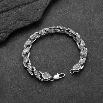 A silver-toned Cuban link chain bracelet with pavé-set clear stones, displayed on a dark textured slate surface.