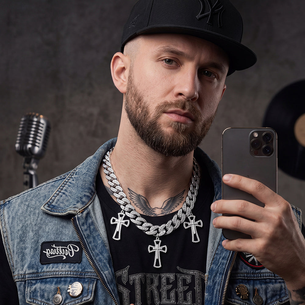 Man with tattoos and jewelry holding a phone, wearing a denim jacket and black cap, with a microphone and vinyl record in the background.