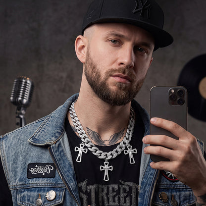 Man with tattoos and jewelry holding a phone, wearing a denim jacket and black cap, with a microphone and vinyl record in the background.