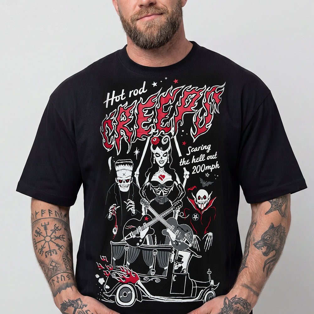 A man wearing a black graphic t-shirt with a detailed red, white, and black design featuring the text 'Hot rod GREEKY' and illustrations of a devil, Frankenstein's monster, and a skull car.