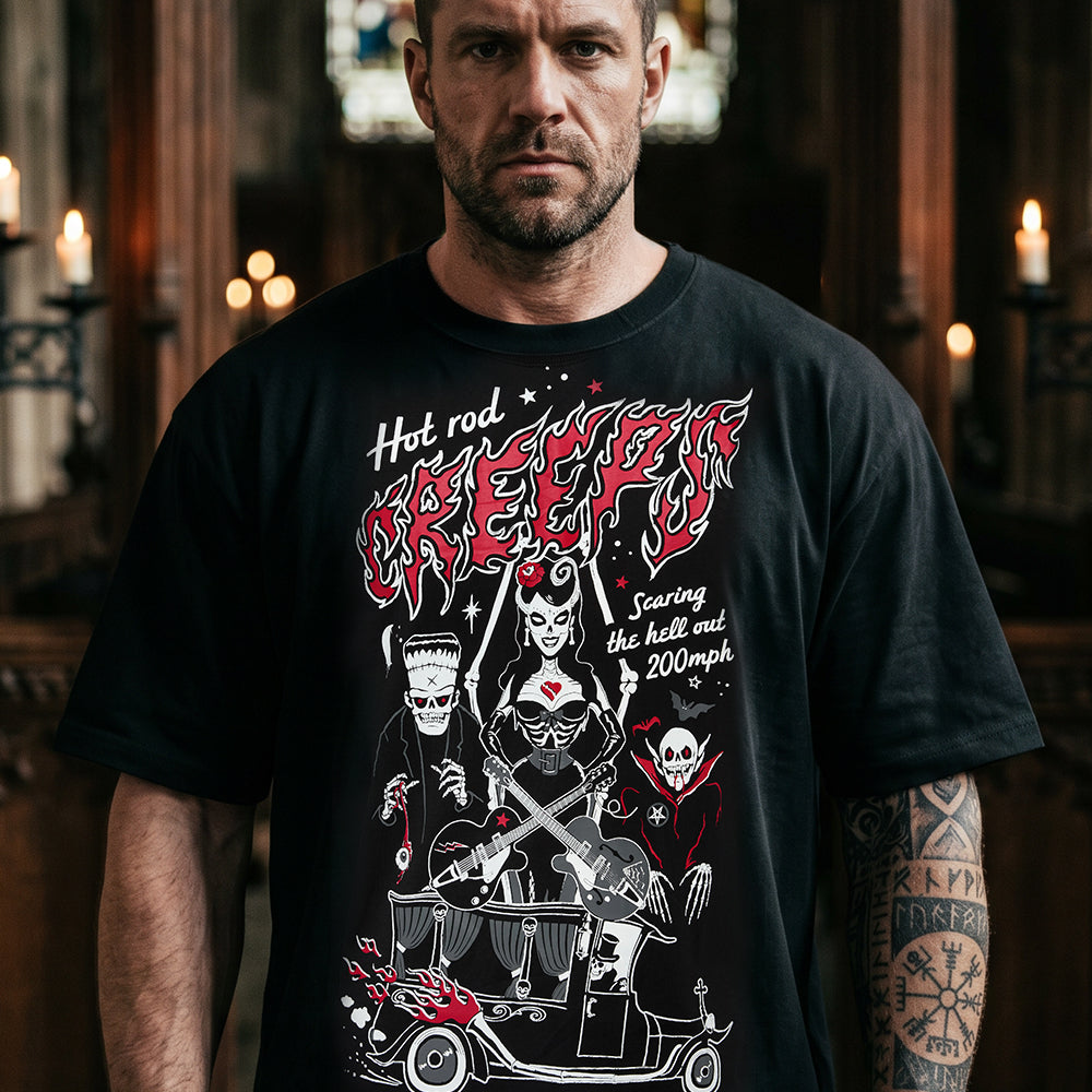 A man wearing a black graphic t-shirt with a red and white 'Hot Rod Creepers' design, standing in a dimly lit, atmospheric room with candles.