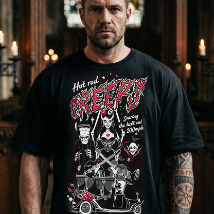 A man wearing a black graphic t-shirt with a red and white 'Hot Rod Creepers' design, standing in a dimly lit, atmospheric room with candles.