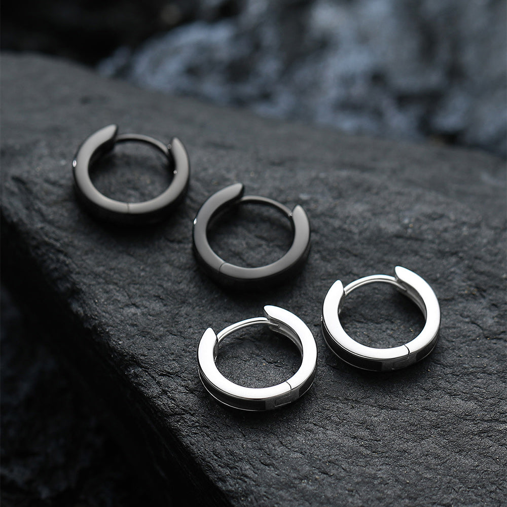 Two pairs of hoop earrings, one black and one silver, on a dark stone surface.