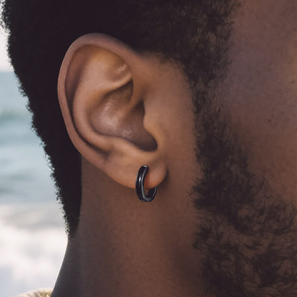 Close-up of an ear with a black hoop earring against a blurred natural background