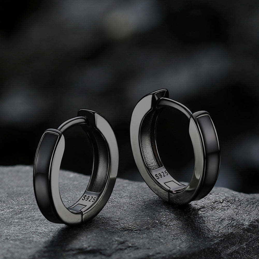 Black hoop earrings on a dark stone surface with a blurred background