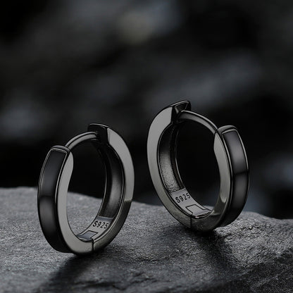 Black hoop earrings on a dark stone surface with a blurred background