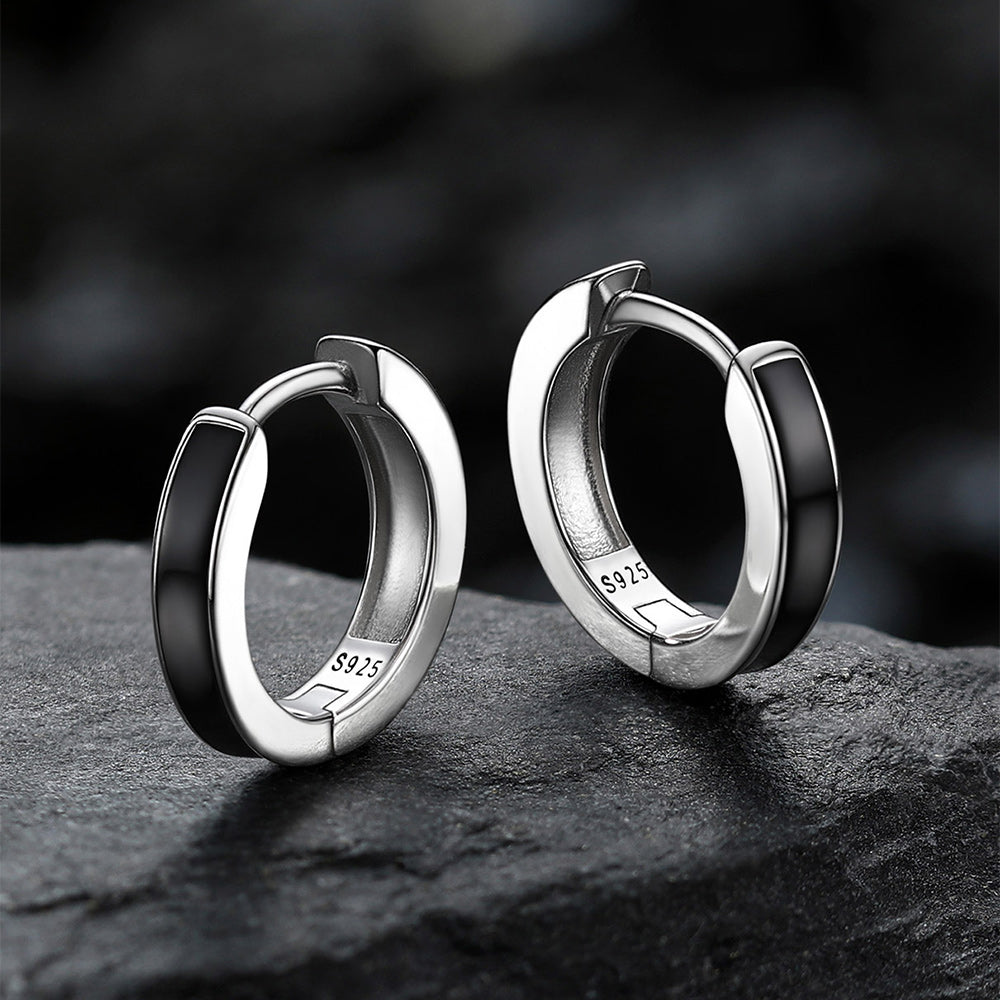 Pair of silver hoop earrings on a dark surface with a blurred background