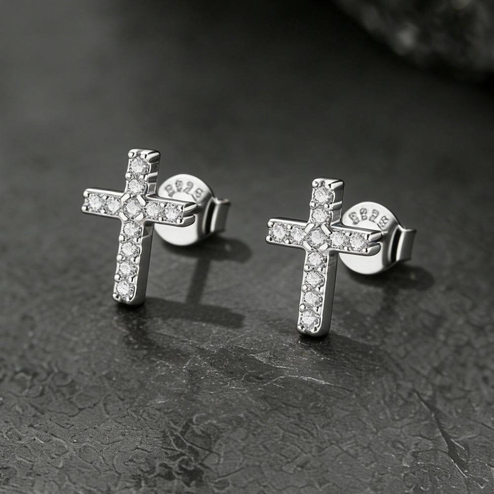 Silver cross earrings with clear stones on a dark textured surface