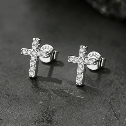 Silver cross earrings with clear stones on a dark textured surface