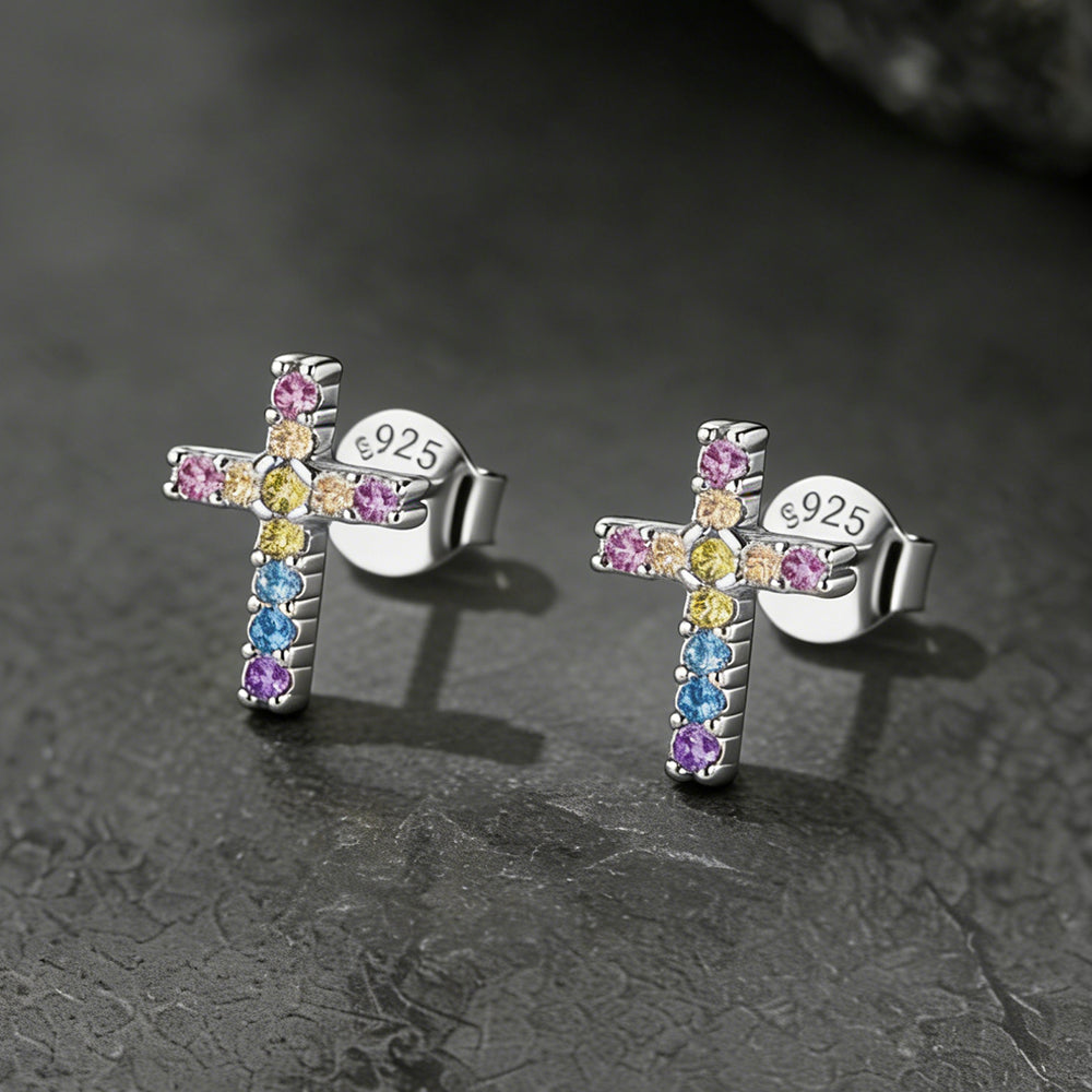 Cross-shaped earrings with colorful gemstones on a dark textured background