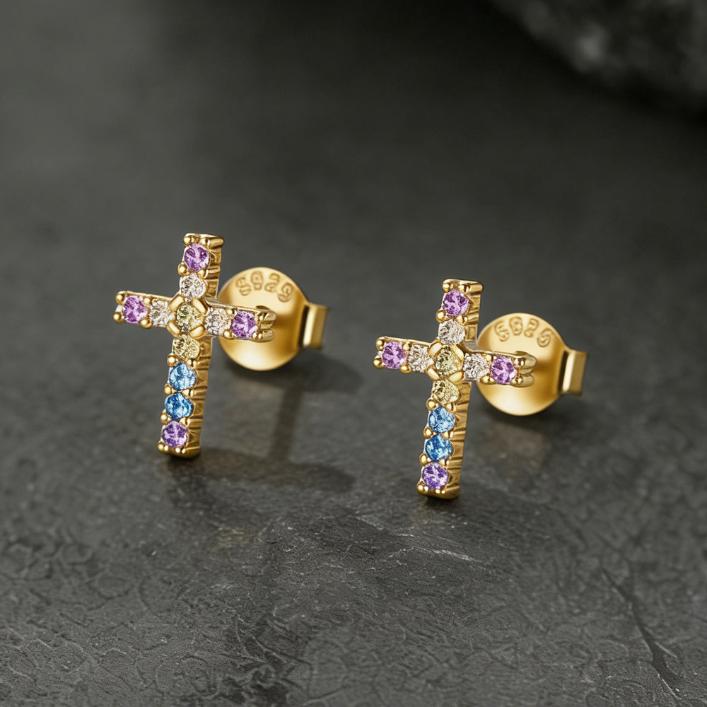 Gold cross earrings with colorful gemstones on a dark textured background