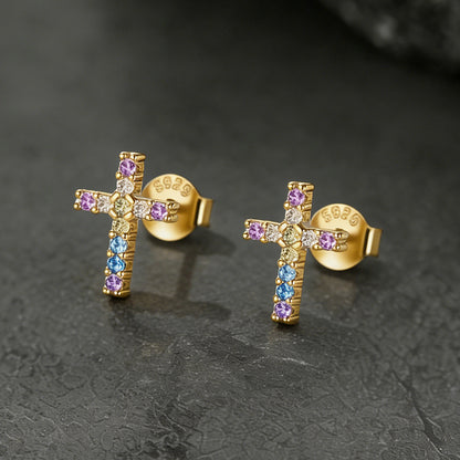 Gold cross earrings with colorful gemstones on a dark textured background