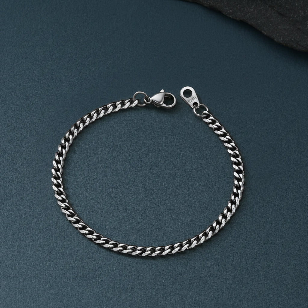 A silver-toned curb chain bracelet with a lobster clasp, displayed on a dark slate-textured surface.
