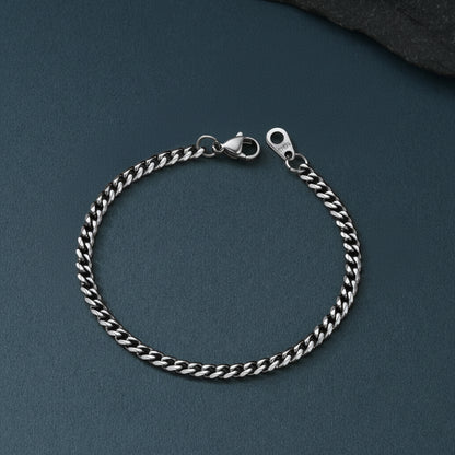 A silver-toned curb chain bracelet with a lobster clasp, displayed on a dark slate-textured surface.