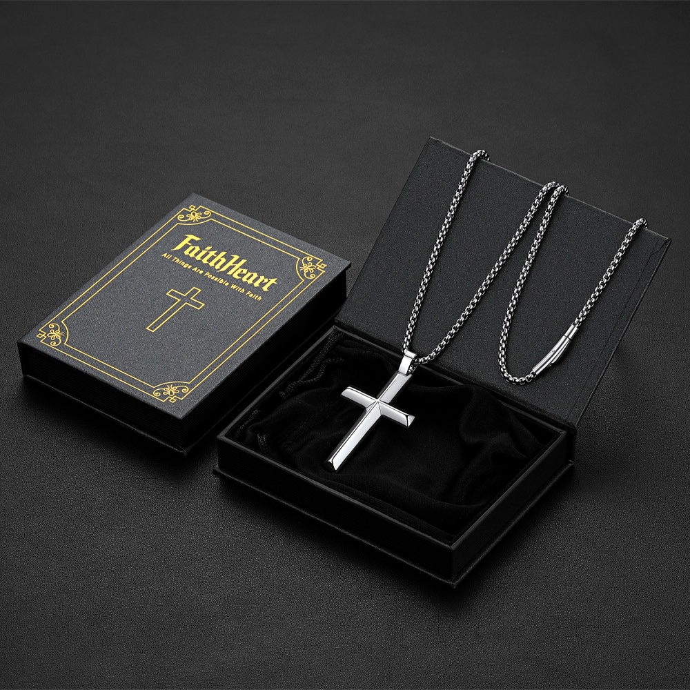 A silver beveled edge cross pendant necklace on a chain, displayed inside an open black presentation box. 