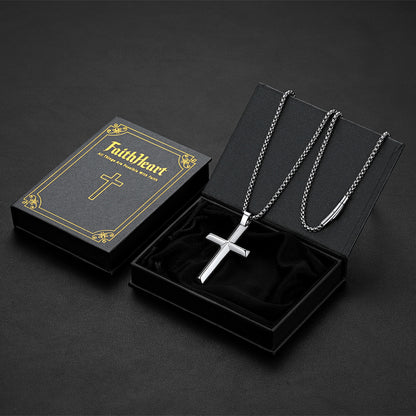 A silver beveled edge cross pendant necklace on a chain, displayed inside an open black presentation box. 