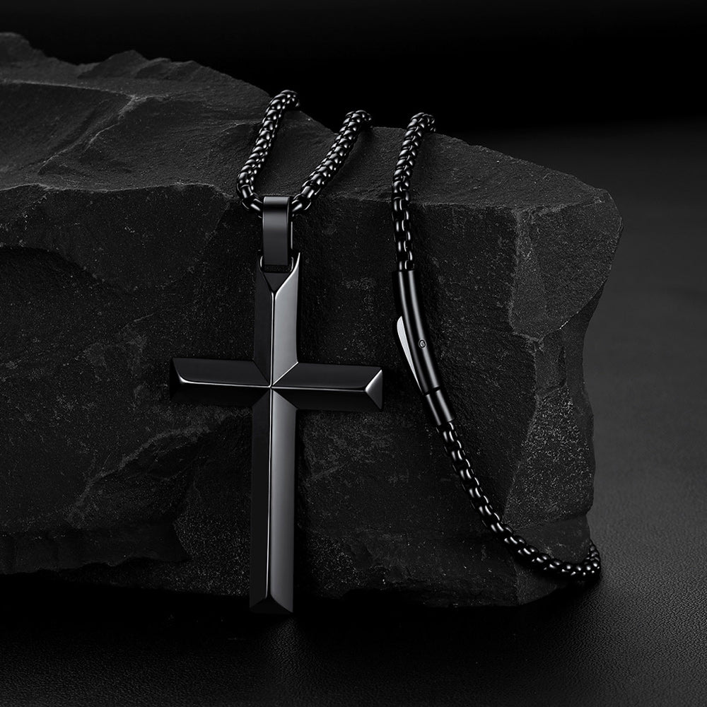 A black beveled edge cross pendant necklace draped over a dark textured rock.