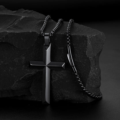 A black beveled edge cross pendant necklace draped over a dark textured rock.