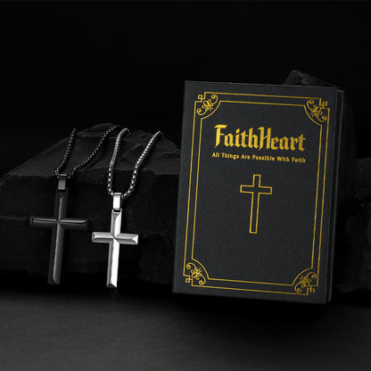 Two beveled edge cross necklaces displayed on a black rock next to a black gift box.