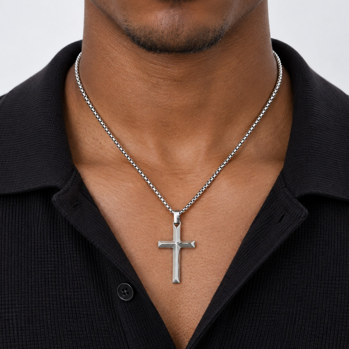 A silver cross pendant necklace on a silver ball chain, worn by a man.