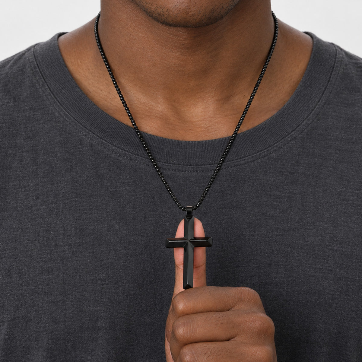 A close-up of a man wearing a black beaded chain necklace with a black cross pendant.