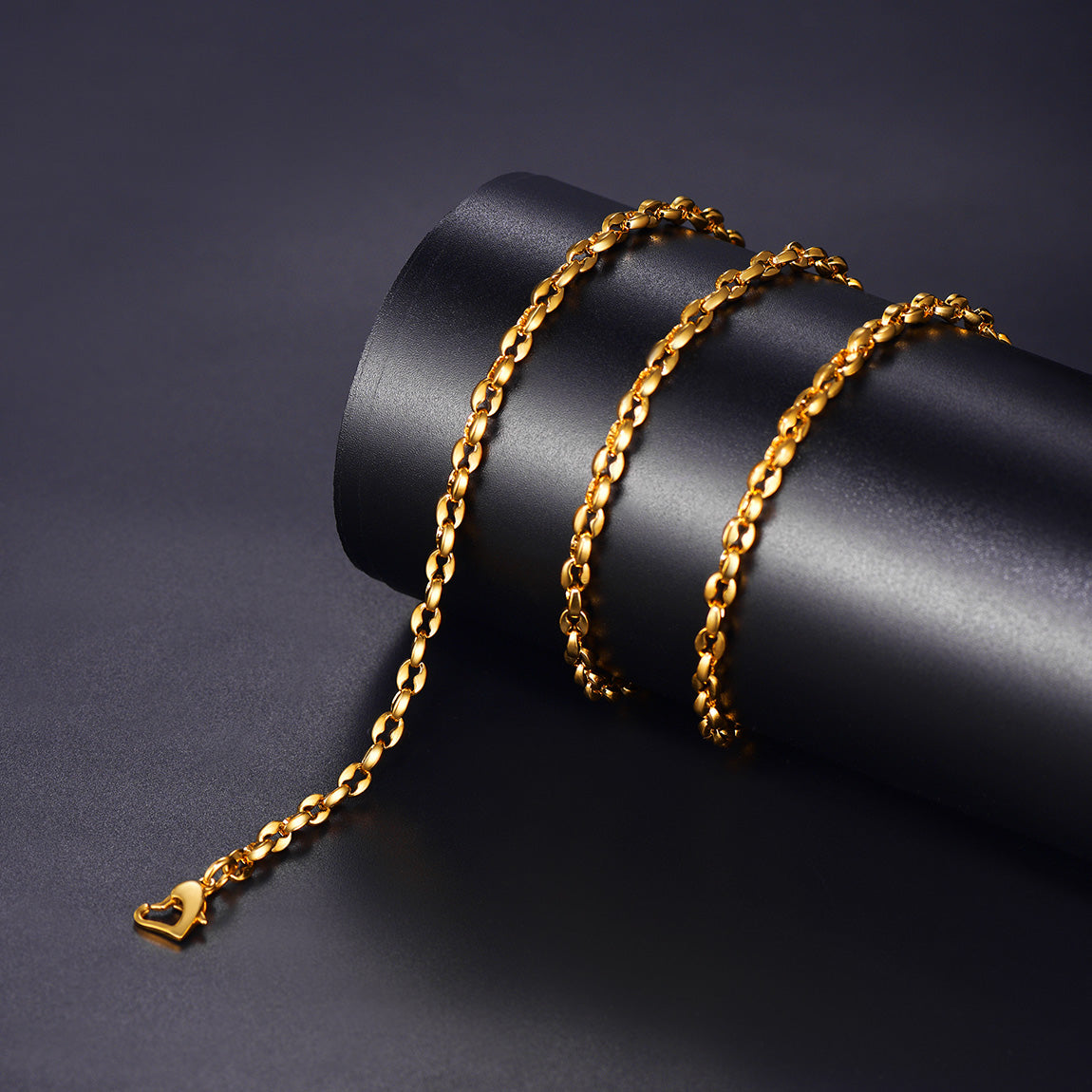 Gold chain bracelet on a dark cylindrical stand with a dark background