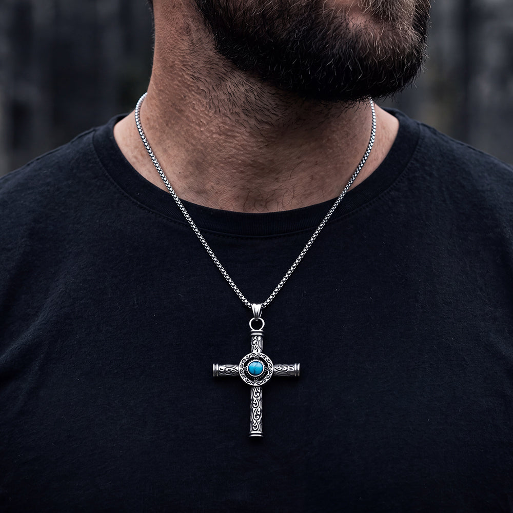 A silver cross pendant necklace with a turquoise center, worn by a man in a black t-shirt.