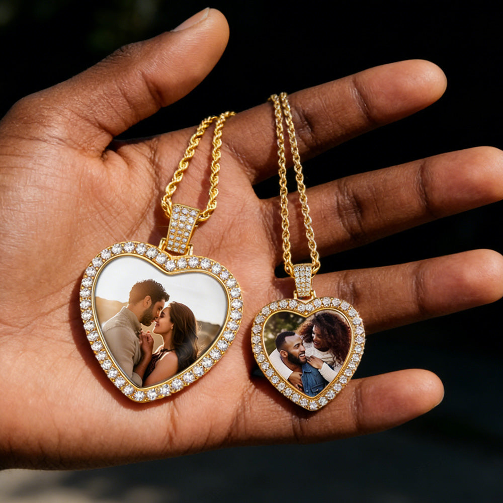 Heart-shaped photo pendants on gold chains held in a hand against a dark background