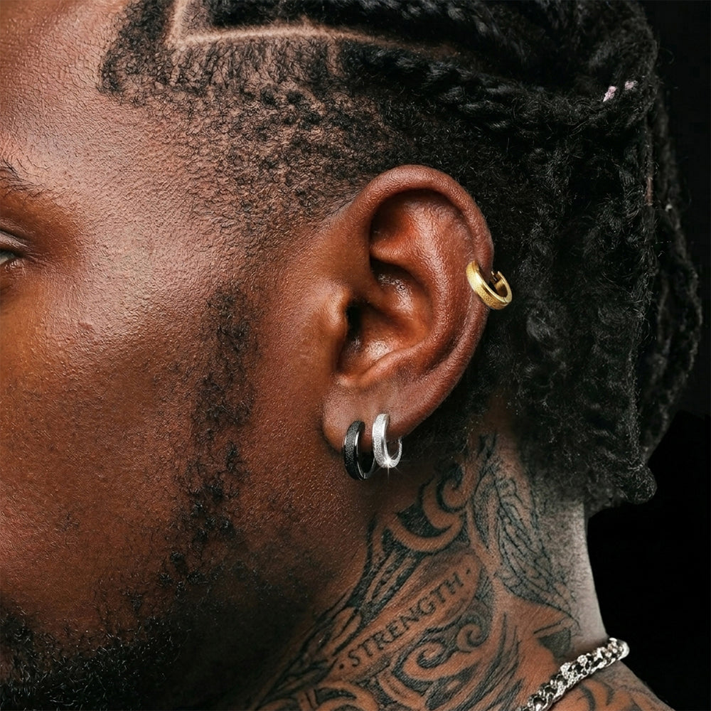 Close-up of a person's ear with earrings and tattoos on a dark background