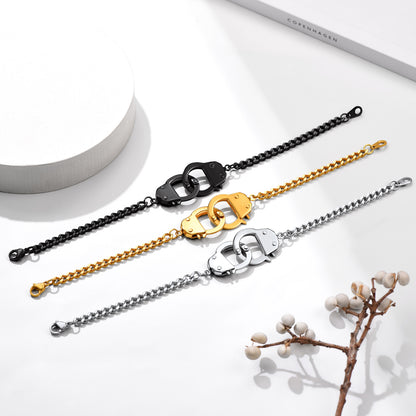 Three chain bracelets in black, gold, and silver on a white surface with a branch and cylindrical object.